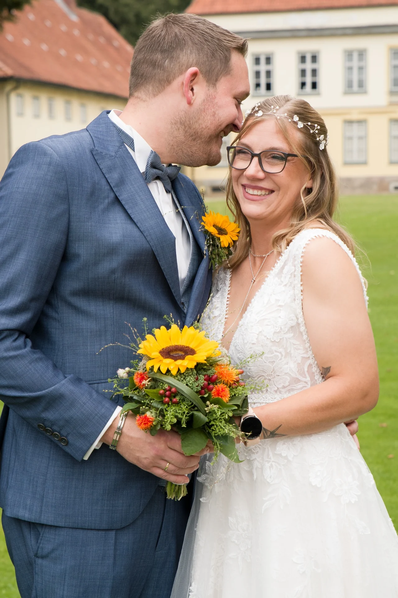Das Hochzeitspaar steht eng beieinander. Die Braut lächelt und hält einen Strauß mit Sonnenblumen.